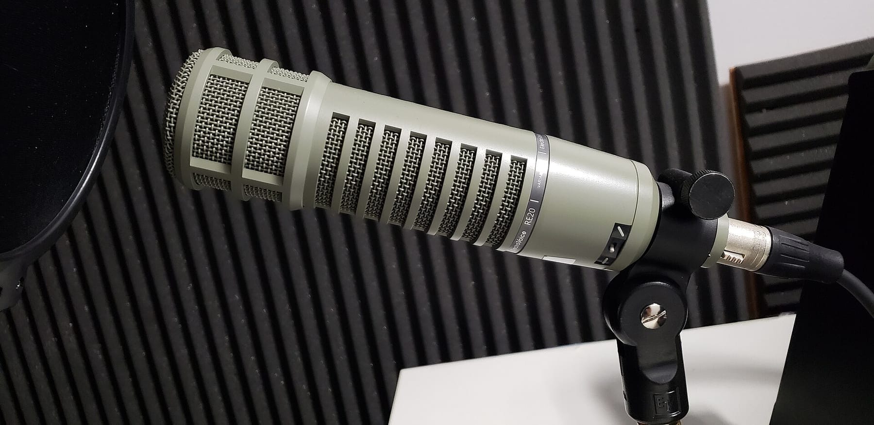 A large broadcast microphone on a boom stand inside a sound-treated voice-over booth